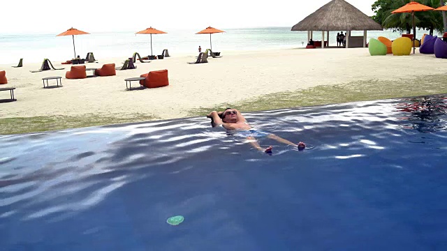 男人躺在可以看到海景的游泳池里视频素材