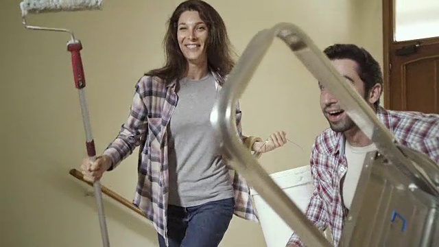 一对年轻夫妇在他们的新房子里拿着粉刷墙壁的工具视频素材
