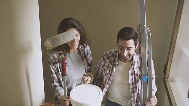 一对年轻夫妇在他们的新房子里拿着粉刷墙壁的工具视频下载