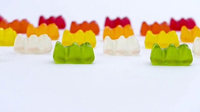 彩色的小熊软糖，甜蜜的水果果冻糖果在白色的背景水平移动。视频下载