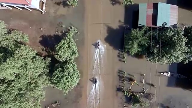 一辆摩托车从头顶飞过，行驶在被洪水淹没的街道上，穿过一个乡村视频素材