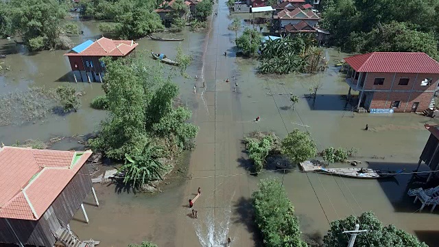 无人机拍摄的摩托车、嘟嘟车和孩子们在被洪水淹没的乡村街道上玩耍视频素材