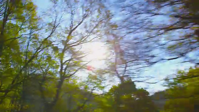在一个美丽的秋日，我们驱车行驶在弯弯曲曲的山路上。从一辆车的侧窗拍摄的POV，手持相机，对着太阳拍摄视频素材