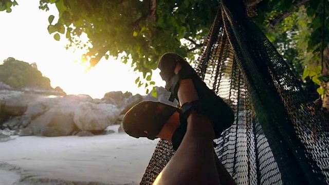 人摇摆和休息在一个吊床下的树在日落海夏季概念视频素材