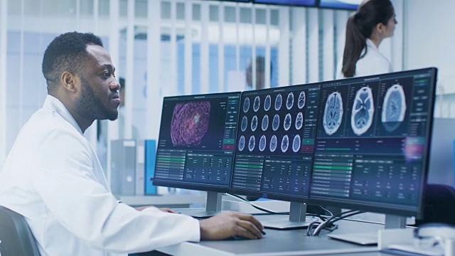 在实验室用个人电脑研究CT大脑扫描图像的医学科学家。神经研究中心的神经学家研究脑肿瘤的治疗方法。视频素材
