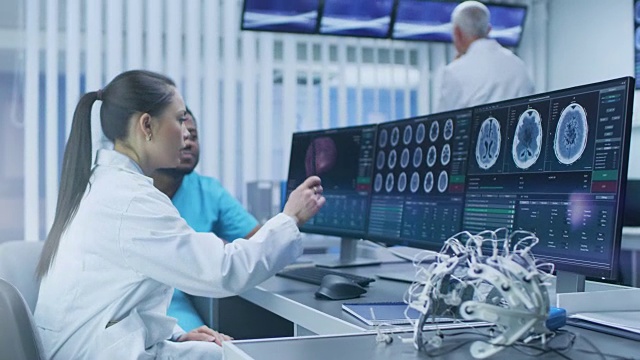 医学科学家和外科医生在实验室用个人电脑讨论CT脑部扫描图像。未来神经研究中心的神经学家/神经科学家致力于脑肿瘤的治疗。视频素材
