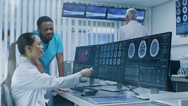 医学科学家和外科医生在实验室用个人电脑讨论CT脑部扫描图像。神经研究中心的神经学家/神经科学家致力于脑肿瘤的治疗。视频素材
