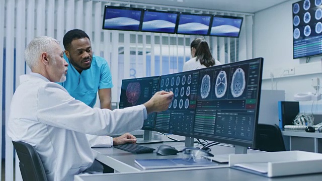 医学科学家和外科医生在实验室用个人电脑讨论CT / MRI脑部扫描图像。神经研究中心的神经学家/神经科学家致力于脑肿瘤的治疗。视频素材