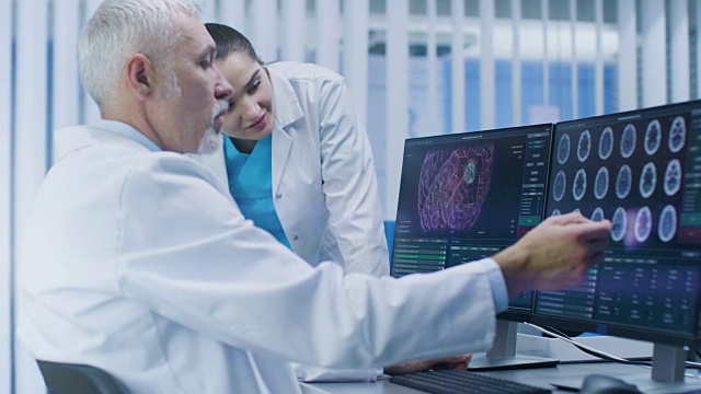 两位医学科学家在实验室用个人电脑讨论CT / MRI脑部扫描图像。神经研究中心的神经学家/神经科学家致力于脑肿瘤的治疗。视频素材