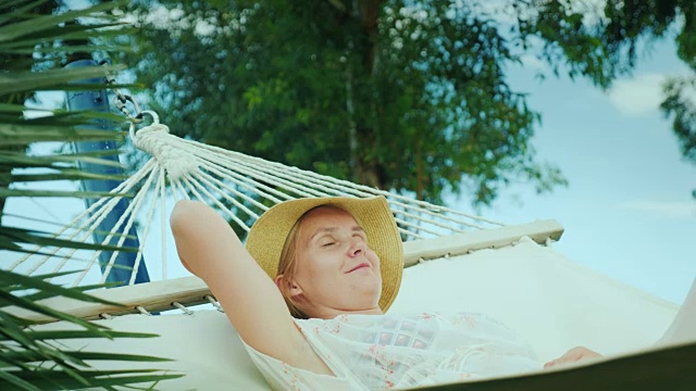 一位年轻女子正在海边度假胜地的吊床上休息视频下载