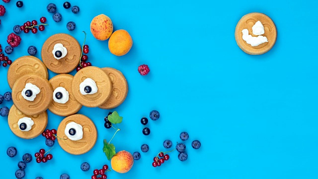停止运动的食物背景。美味的迷你微笑煎饼与浆果在蓝色表面，俯视图，动态场景，4k视频视频下载