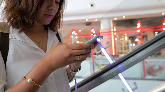 美丽的年轻女子迷人的近距离在商场扶梯上使用移动智能手机在购物中心视频素材