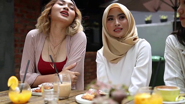 戴着头巾的女人和她的朋友在咖啡厅喝果汁视频素材