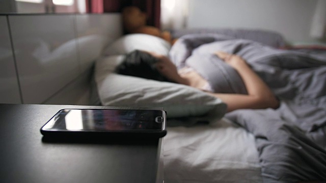 一个正在床上睡觉的女人被手机闹铃吵醒了视频素材
