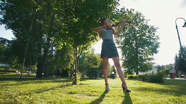 日落时分，一个年轻女子站在公园的草地上拉小提琴视频素材
