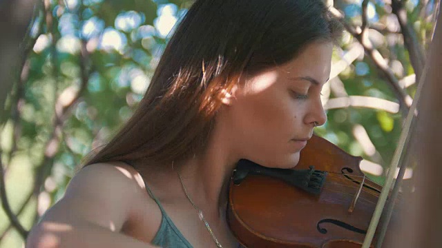 夏日里年轻的潮女人在户外拉小提琴的肖像视频素材