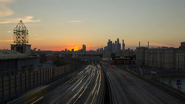前景是宽阔的城市高速公路上密集的车流，背景是日落与办公大楼附近的云移动视频素材