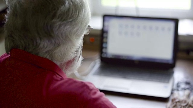 一个老人坐在家里的桌子旁用笔记本电脑视频素材