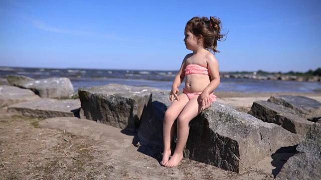 可爱的孩子坐在岩石海滩上视频素材