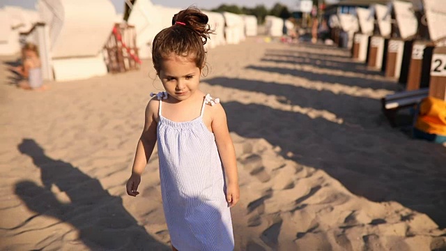 漂亮的蹒跚学步的孩子穿着裙子在海滩上散步视频素材