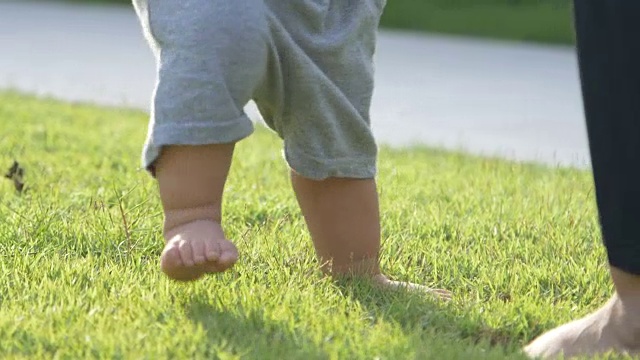 小男孩学着在绿草地上走路，迈出他的第一步，妈妈牵着他的手视频素材