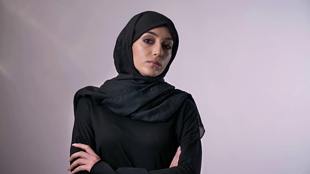 年轻自信的穆斯林女孩戴着头巾，双臂交叉，看着镜头，宗教观念，灰色背景视频下载