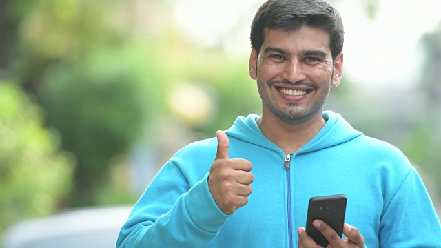 年轻快乐的波斯男人在户外用电话和竖起大拇指视频素材