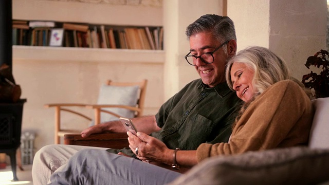 相爱的老年夫妇使用智能手机，在家里一起大笑视频素材
