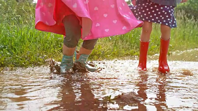 两个小女孩在一个泥泞的水坑里跳着，微笑着视频素材