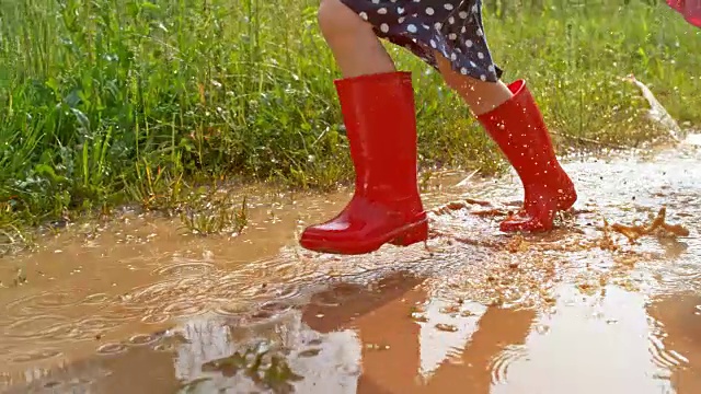 小女孩穿着红色雨靴跑过一个泥泞的水坑视频下载
