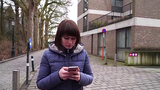 在比利时布鲁日散步的女孩，看着智能手机视频素材