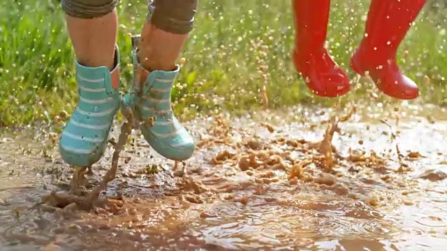 SLO MO两个小孩的腿在泥泞的水坑里跳上跳下视频下载