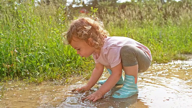 小女孩在泥泞的水坑里玩她的手视频素材