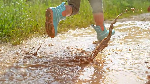一个穿着雨靴的小孩的腿跑过泥泞的水坑视频下载
