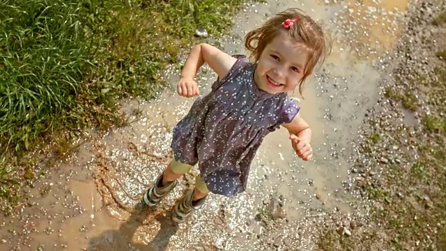 小女孩穿着雨靴在水坑里跳上跳下，笑着视频下载