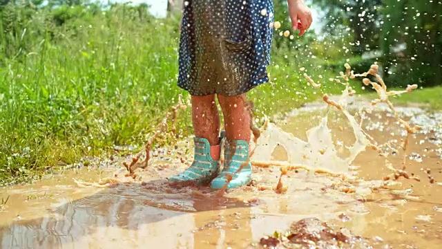 小女孩穿着多蒂裙子和雨靴，在泥泞的水坑里跳来跳去，浑身是泥视频下载