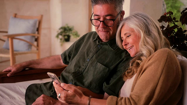 幸福的成熟夫妇使用智能手机，在家里一起放松视频素材