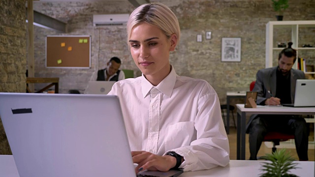 年轻快乐的女商人正在办公室的笔记本电脑上打字，同事们正在用技术联网，工作理念，交流理念视频素材