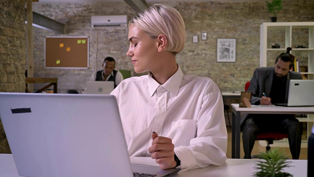 年轻快乐的女商人正坐在办公室的笔记本电脑前跳舞，同事们都在用科技联网，工作理念，放松理念，交流理念视频素材