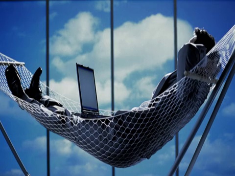 放松和无忧无虑的商人躺在吊床上，膝上放着笔记本电脑视频素材