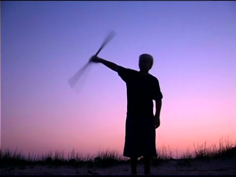 日落时分，少年在海滩上旋转木棍视频下载