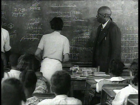 1939 MS老师站在课前，学生举手，一个学生站着走到黑板前，其他学生正在黑板前工作视频素材