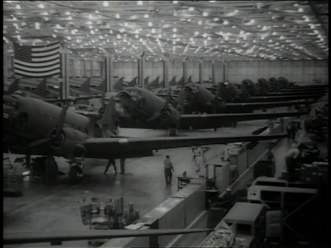 1942年11月，美国加利福尼亚州长滩，工人们在飞机工厂周围走动，中间是一排部分组装的C-47达科塔飞机，后墙上挂着一面美国国旗视频下载