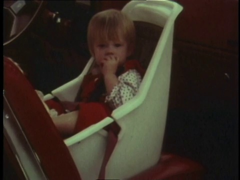 1978年WS蹒跚学步的孩子坐在汽车前面的白色座椅上，面朝后视频素材