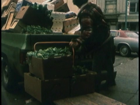 1978蒙太奇快递员在街边市场卸货，堆放食品，同时语音播报当天的市场价格/美国视频下载