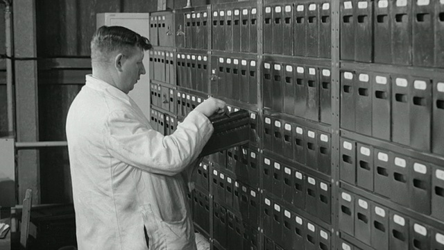 1969蒙太奇技术人员在一排排的文件柜中寻找和打开盒式保险丝/英国视频下载