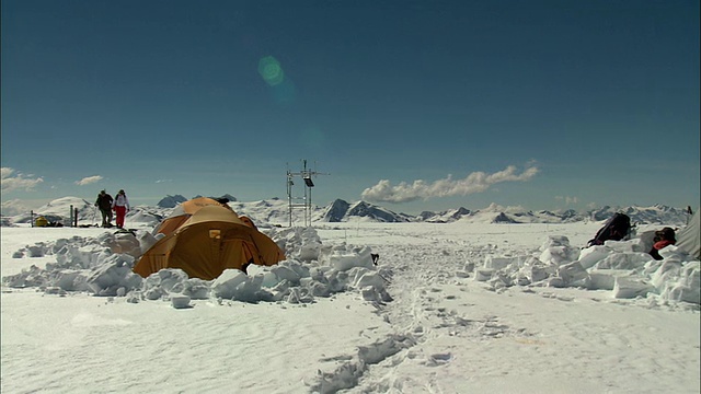 徒步旅行者穿过雪走向一个科学基地营地，雪中有仪器视频素材