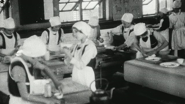 1925年，蒙太奇女学生戴着帽子和围裙在家庭经济课上准备和烹饪食物和摆餐桌/纽卡斯尔泰恩，英国视频素材