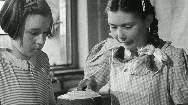 1950蒙太奇在他们面前的岛上，一名厨师和一名儿童观察一名小女孩在蛋糕上涂糖霜，蛋糕烘焙的残余在他们面前/英国视频下载