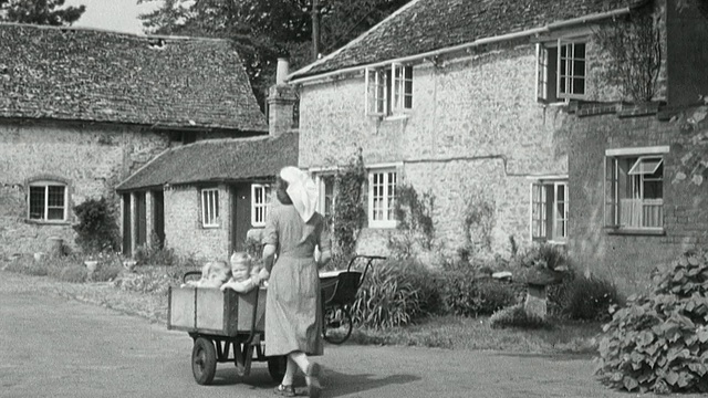 1950年，英国儿童福利院的保姆推着手推车，带着蹒跚学步的孩子穿过大门，转过街角，走下小巷视频下载